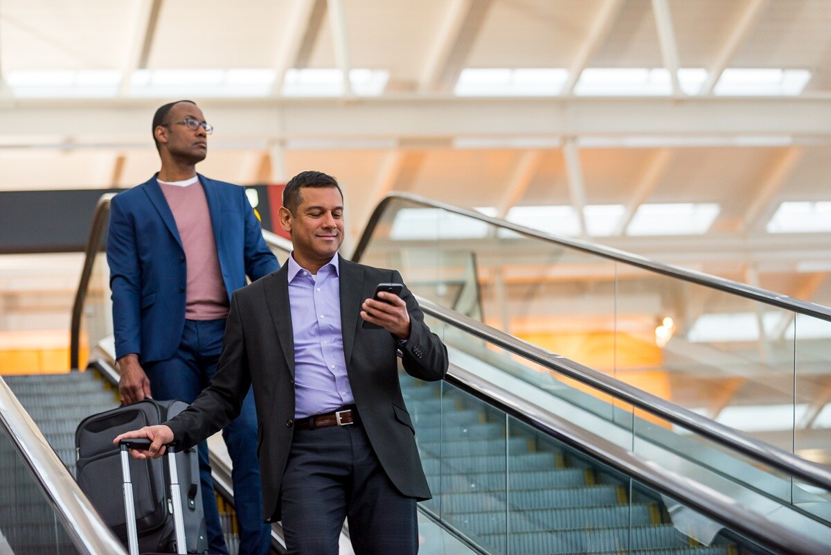 Two men on business trip coming down escalator in airport