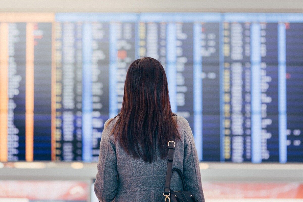 Lady with long dark hair standing in front of departure board 