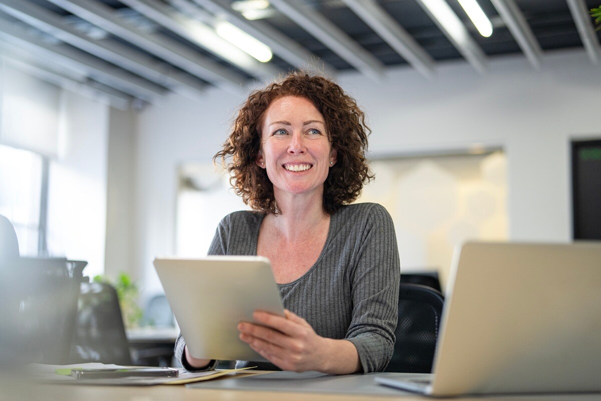 Lady in grey top sitting at desk holding tablet