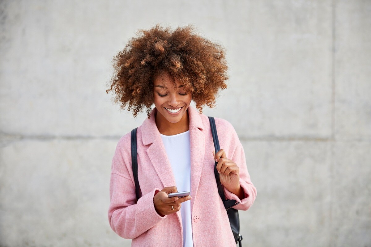 Woman in pink jacket looking at phone smiling 