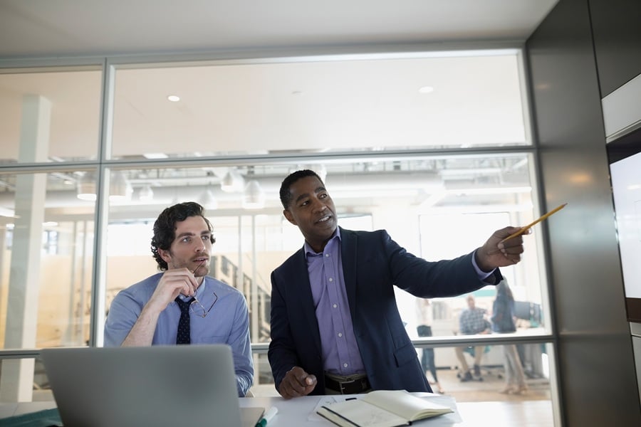 Two men in glass office looking at whiteboard