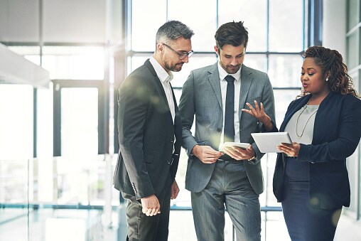 Three people standing in office looking at tablet