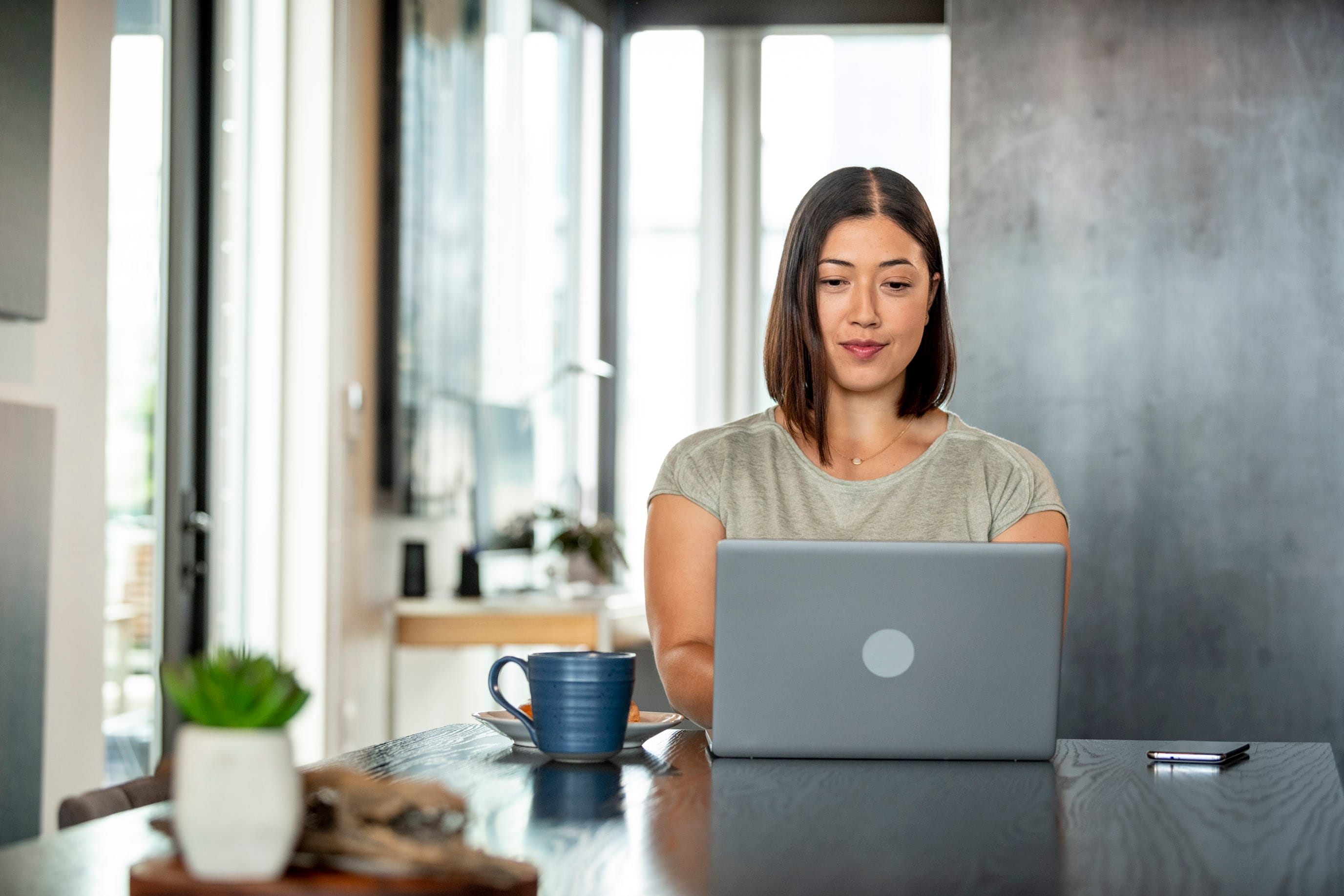 Lady sitting in front of laptop with blue coffee mug on desk next to her