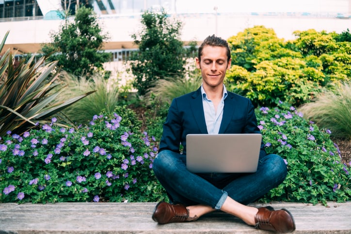 Man sitting on floor with laptop in front of purple flowers 