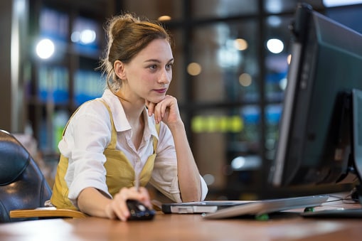Lady in white shirt with waistcoat looking at computer hand on mouse