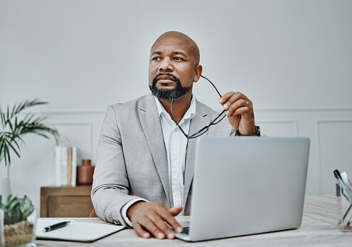 Smartly dressed man, sitting behind laptop with his glasses in his hand