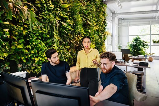 three people standing around desk in office