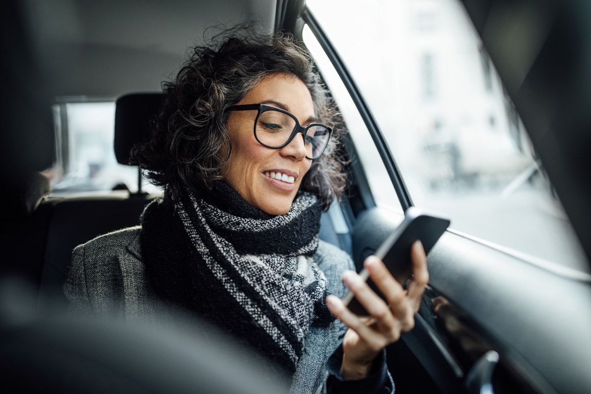 Lady in car wearing glasses, looking at her phone 