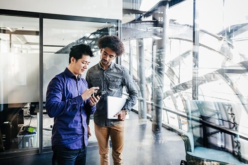 Two men in glass office looking at a phone