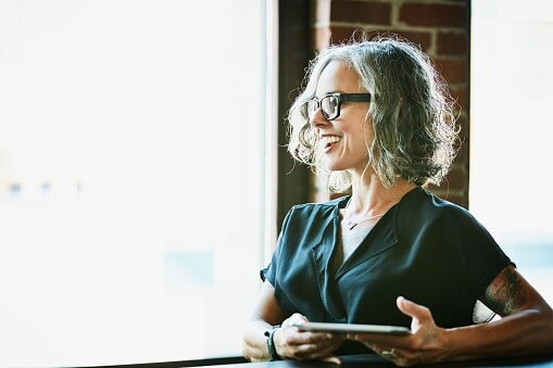 Lady with grey hair and glasses in black shirt holding a table 