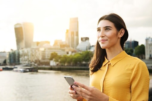Lady in yellow dress with long hair standing in front of city