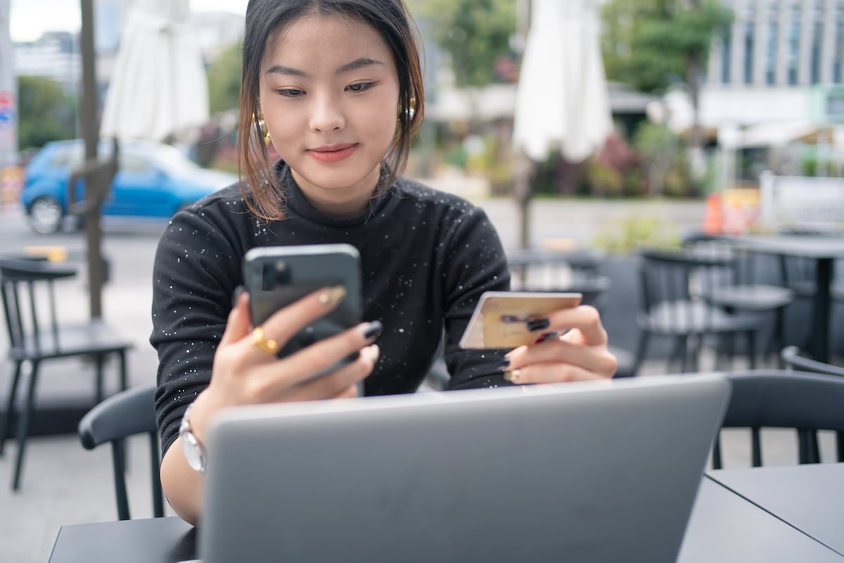 woman holding credit card and phone, while and computer